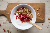 Yoghurt with granola and pomegranate seeds in bowl with wooden spoon — Stock Photo