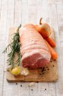 Uma junta crua de porco com uma cebola, cenouras, alecrim e especiarias em uma tábua de cortar — Fotografia de Stock