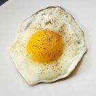 Жареное яйцо с черным перцем на белой тарелке — стоковое фото