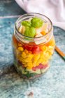 Una ensalada colorida en un frasco de vidrio con quinua roja, pepino, pimientos, maíz, tomates, pecorino y albahaca - foto de stock
