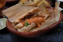Tamales veganos rellenos de seitán, masa, chile verde y servidos con salsa ranchero, nata y chile - foto de stock
