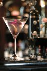 Джинний коктейль, прикрашений рожевою орхідеєю, подається в келиху мартіні в барі — стокове фото