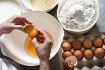 Mãos quebrando ovos sobre uma tigela com farinha de amêndoa e farinha regular com fermento em pó ao lado — Fotografia de Stock