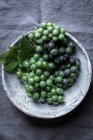 Uvas frescas recogidas en tazón de cerámica sobre mantel gris - foto de stock