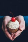 Mãos segurando um cupcake com cobertura de amendoim e uma cereja de coquetel — Fotografia de Stock