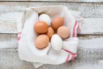Chicken eggs in tea towel on wooden background — Stock Photo