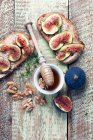 Bread toasts with figs, honey, walnuts and thyme on rustic wooden surface — Stock Photo