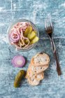 Колбаса, красный лук и салат из огурцов в стеклянной банке с ломтиками багета — стоковое фото