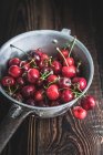 Wet cherries in metal colander on wooden surface — Stock Photo