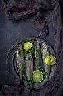 Fresh sardines with slices of lime on a metal plate (seen from above) — Stock Photo