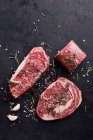 Various beef steaks with herbs and spices on a black background — Stock Photo
