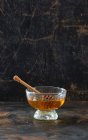 Miel con una cuchara de miel en un recipiente de vidrio frente a un fondo oscuro - foto de stock