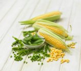 Petit pois and corn on the cob on a wooden background — Stock Photo