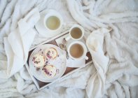Cupcakes à la vanille avec thé sur un plateau sur une couverture blanche confortable (vue d'en haut) — Photo de stock