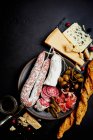 Una bandeja antipasti mixta con aceitunas, alcaparras, jamón, salchichas secas, salami, grissini, parmesano y queso azul - foto de stock