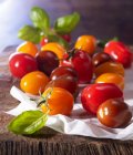 Diferentes tipos de mini tomate con albahaca sobre papel y una tabla de madera - foto de stock