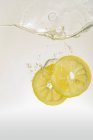 Лимонные ломтики падают в воду — стоковое фото