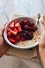 Hand holding bowl of porridge with jam, fresh raspberries and strawberries — Stock Photo
