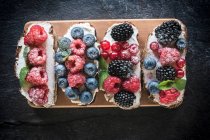 Брушеттас з ягодами та вершковим сиром на дерев'яній дошці — стокове фото