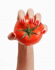Une main de femme avec des ongles rouges tenant une tomate — Photo de stock