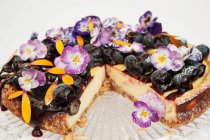Bolo de queijo de mirtilo em um suporte de bolo de vidro decorado com flores de Pansy e pétalas de calêndula — Fotografia de Stock