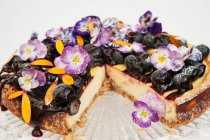 Blueberry cheese cake on a glass cake stand decorated with Pansy flowers and Marigold petals — Stock Photo