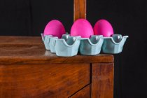 Pink Easter eggs in an egg carton on a wooden chair — Stock Photo