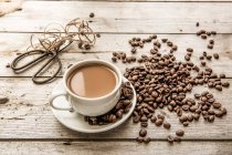 Caffè bianco in una tazza e chicchi di caffè con forbici e spago sullo sfondo — Foto stock