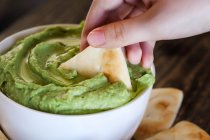 Woman's hand dipping pita bread into vegan avocado hummus — Stock Photo
