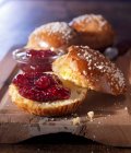 Brioche buns on wooden board, one sliced open, with sugar crystals and raspberries jam — Stock Photo