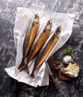 Three smoked mackerels on paper with salt and buttered bread — Stock Photo