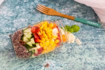 Красочный салат в стеклянной банке с красным киноа, огурцом, перцем, кукурузой, помидорами, пекорино и базиликом, с деревянной вилкой — стоковое фото