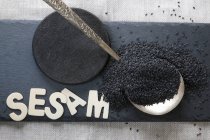 Black sesame seeds on a silver spoon and wooden letters on a slate plate — Stock Photo