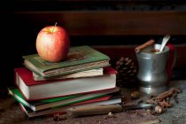 Uma maçã rosa em uma pilha de livros antigos com suco de maçã quente — Fotografia de Stock