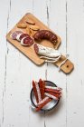 Différentes saucisses espagnoles dans un plat en émail et sur une planche en bois (vue du dessus) — Photo de stock