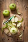 Manzanas Bramley verdes, enteras y peladas, con pelador de manzanas - foto de stock