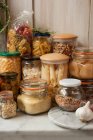 Arreglo de naturaleza muerta en una despensa de tarros de almacenamiento del pasado, nueces, mermeladas, aceitunas, frutas y lentejas, en una despensa en un estante de mármol - foto de stock