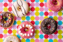 Bunt dekorierte Donuts auf einer gepunkteten Tischdecke (Ansicht von oben)) — Stockfoto