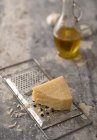 Pièce de parmesan sur râpe à fromage métallique avec cruche à huile sur fond — Photo de stock