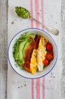Миска для сніданку з авокадо та огірковим кремом, яєчнями, беконом та помідорами — стокове фото