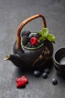 Eine Teekanne mit frischen Beeren und Teeblättern — Stockfoto