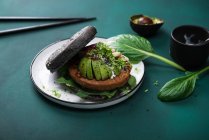 Sojaproteinpatty mit Avocado, Radieschen und zwei Soßen in einem schwarzen Burger-Brötchen — Stockfoto