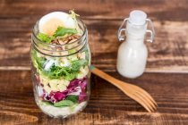 Orzo pasta with lambs lettuce, radicchio, endive, croutons, cheese, walnuts and eggs in a glass jar with dressing and a wooden fork — Stock Photo