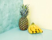 Ganze Ananen und Bananenbündel auf gelbem und grünem Hintergrund — Stockfoto