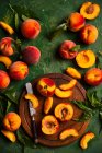 Fresh peaches with leaves on wooden board with knife and on green surface — Stock Photo