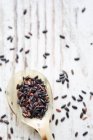 Black rice on a spoon and a wooden background (seen from above) — Stock Photo