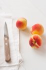 Три абрикоси з тканиною і ножем на білій поверхні — стокове фото