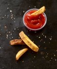 Four French fries on a black baking tray with tomato ketchup — Stock Photo