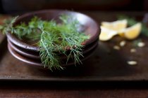 Fresh dill fronds in a wood bowl and lemon wedges — Stock Photo