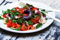 Octopus salad with tomatoes, parsley and white beans on plate with cutlery — Stock Photo